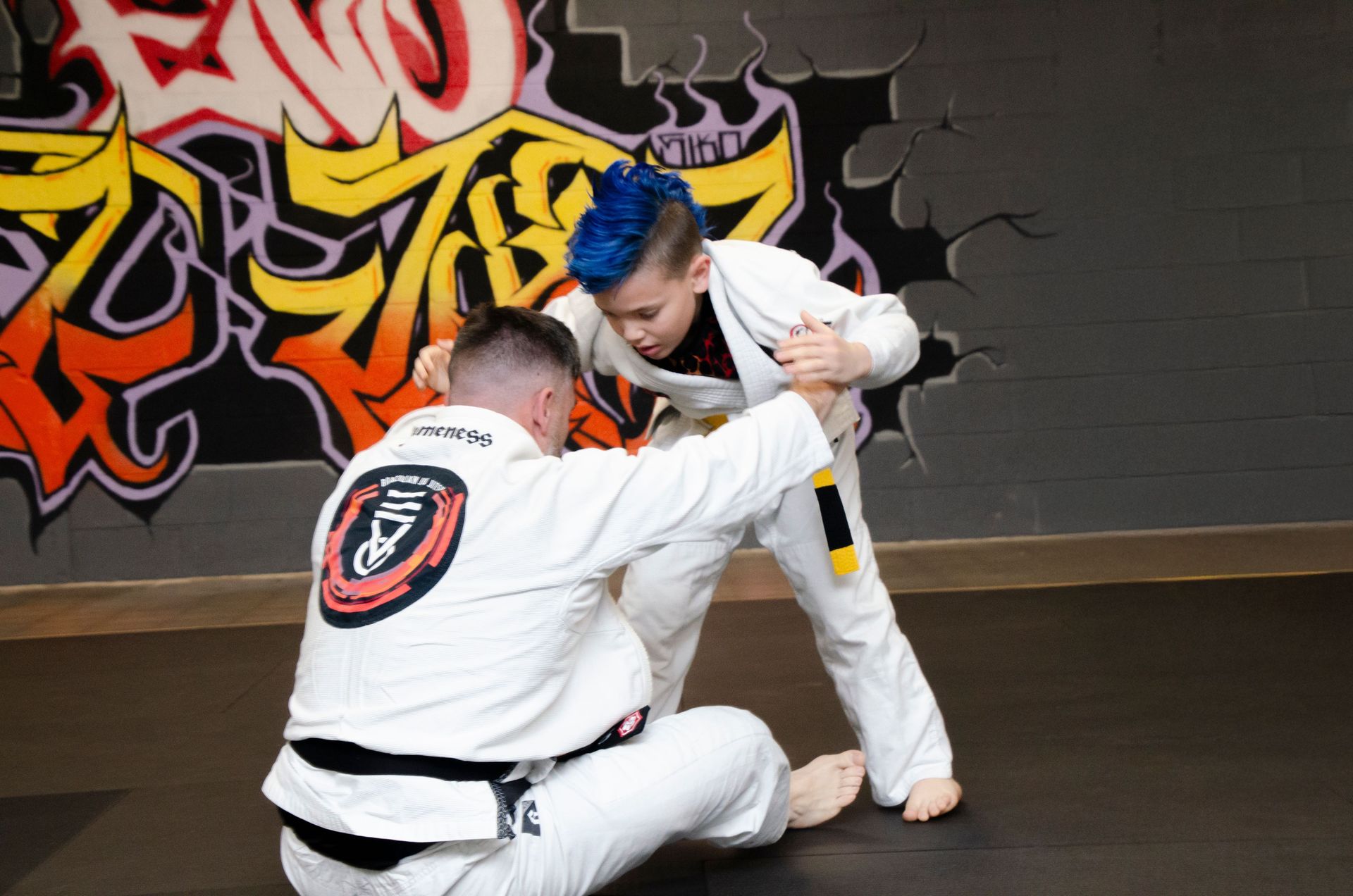 A black belt instructor guiding a young student through a grip on the mats at Second Grip Jiu Jitsu in Carlsbad, New Mexico